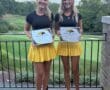 Two girls smiling with golf certificates, wearing matching outfits at a golf course, celebrating their achievements.