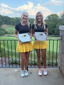 Two girls smiling with golf certificates, wearing matching outfits at a golf course, celebrating their achievements.