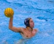 Water polo player in action holding a yellow ball, wearing a numbered cap in a pool.