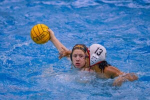 Two water polo players in action, one holding a yellow ball, competing in a swimming pool.