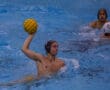 Water polo player poised to throw a yellow ball during a competitive match in a swimming pool.