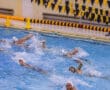Water polo players competing in an action-packed match in an indoor pool with referee watching.
