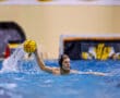 Water polo player prepares to throw ball in action-packed game, creating splash in pool.