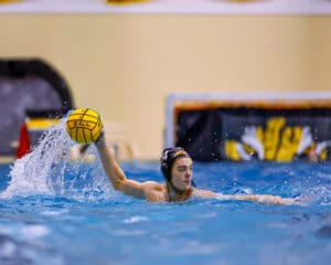 Water polo player prepares to throw ball in action-packed game, creating splash in pool.