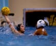 Water polo match action with player holding ball, defending opponent in pool.