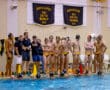 Water polo team strategizes poolside, coach giving instructions, preparing for upcoming game. Championship banners in background.