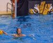 Water polo player in blue pool holding yellow ball, tiger logo in background.