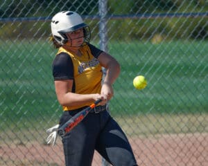 Softball player in yellow jersey batting during a game on a sunny day.