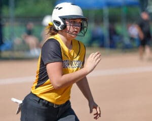 Softball player in yellow jersey running on the field during a game, wearing a helmet and focused on the action.