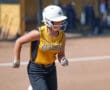 Softball player in yellow jersey runs on the field during a game, wearing a white helmet and gloves.