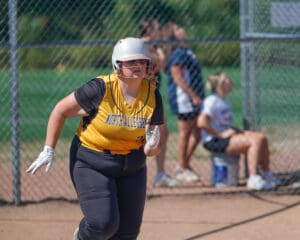 Softball player in yellow jersey running on the field during a game, with a focused expression.