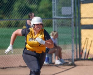 Softball player in yellow jersey runs during a game, capturing action and focus on the field.