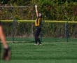 Softball player catches fly ball at outfield fence in mid-game action.