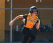 Softball player in action wearing a helmet and yellow jersey, North Allegheny team, sprinting on the field.