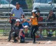 Softball player swings at a pitch during a game with catcher and umpire watching closely.