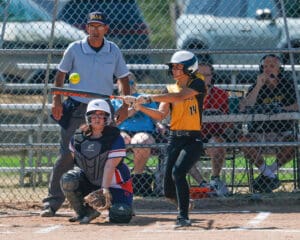 Softball player swings at a pitch during a game with catcher and umpire watching closely.