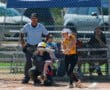 Softball batter swings at a pitch during a game, with an umpire and catcher in position behind the plate.
