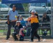 Softball player hits the ball during a game, with catcher and umpire watching closely.