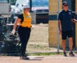 Softball player in yellow jersey at base with coach nearby, chain-link fence in background.