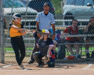 Softball player in action, hitting the ball during a game with umpire and catcher watching.