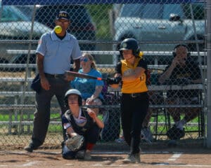 Softball player swinging bat during game with umpire and catcher, sunny field, action shot.