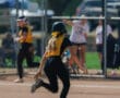 Softball player in yellow running bases during a game on a sunny day.