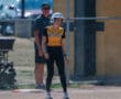 Softball player in North Allegheny uniform stands on base near coach, wearing helmet during daytime game.