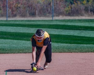 Softball player in yellow jersey fielding a ground ball on a sunny field.
