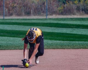 Softball player fielding a ground ball on a sunny day, focused on the game.