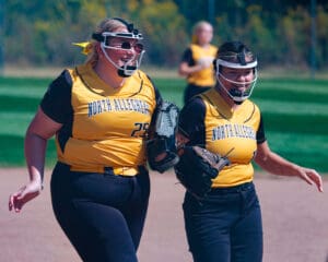 Softball players in North Allegheny uniforms smiling and walking on the field during a game.