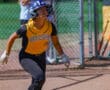 Softball player in yellow jersey and helmet prepares to run at a game, with spectators in the background.