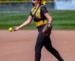 Softball player in action on the field, wearing a yellow and black uniform, preparing to throw the ball.