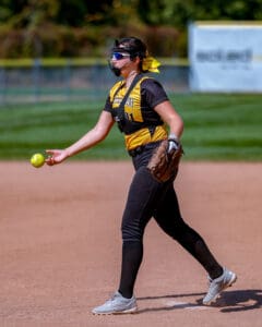 Softball player in action on the field, wearing a yellow and black uniform, preparing to throw the ball.