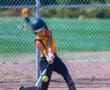 Softball player in action, swinging bat at ball on field with chain-link fence background.
