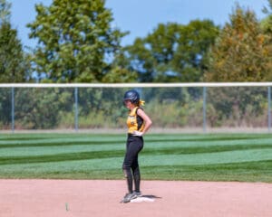 Softball player in helmet stands on second base during a game on a sunny day.