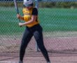 Softball player in a yellow jersey prepares to swing at a pitch on a sunny day.