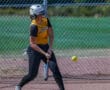 Softball player in yellow jersey preparing to swing at a pitch on a sunny day.