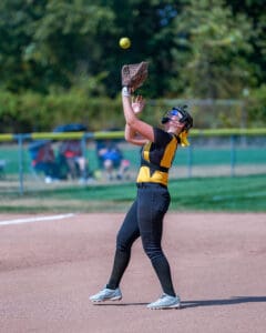 Softball player catching a ball during a game on a sunny field.