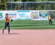 Softball player throws ball on field during game, summer sports action.