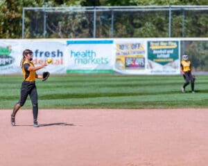 Softball player throws ball on field during game, summer sports action.