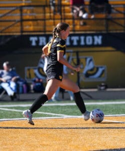 Soccer player dribbling ball on sunny field in action-packed match.