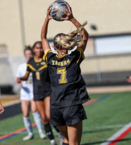 Soccer player in black jersey throws ball during game on green field, focus on action and movement.