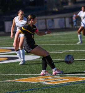 Soccer player in black and yellow uniform kicks ball during game on green field.