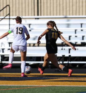 Two soccer players in action on the field, one in white and the other in black, competing for the ball.