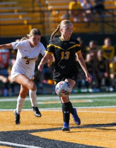 Two women playing soccer on a field, focused on the ball and competing for possession during a match.