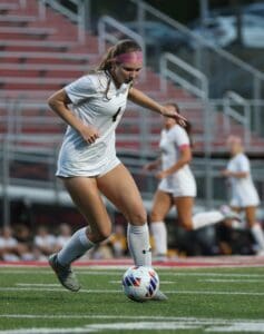 Female soccer player dribbling ball on field during match, focused and determined.