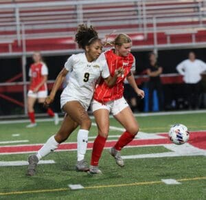 Soccer players competing for the ball during a high school game on a vibrant green field.