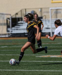 Soccer player in black and yellow uniform dribbling ball on field during match.