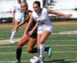 Girls playing soccer on a field, one in black and one in white, focusing on the ball during a match.