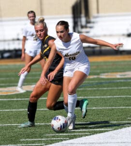 Girls playing soccer on a field, one in black and one in white, focusing on the ball during a match.